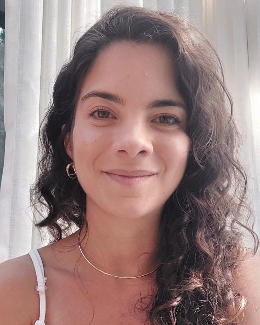 Luana Bilro, psicóloga, sorrindo diante de uma cortina clara